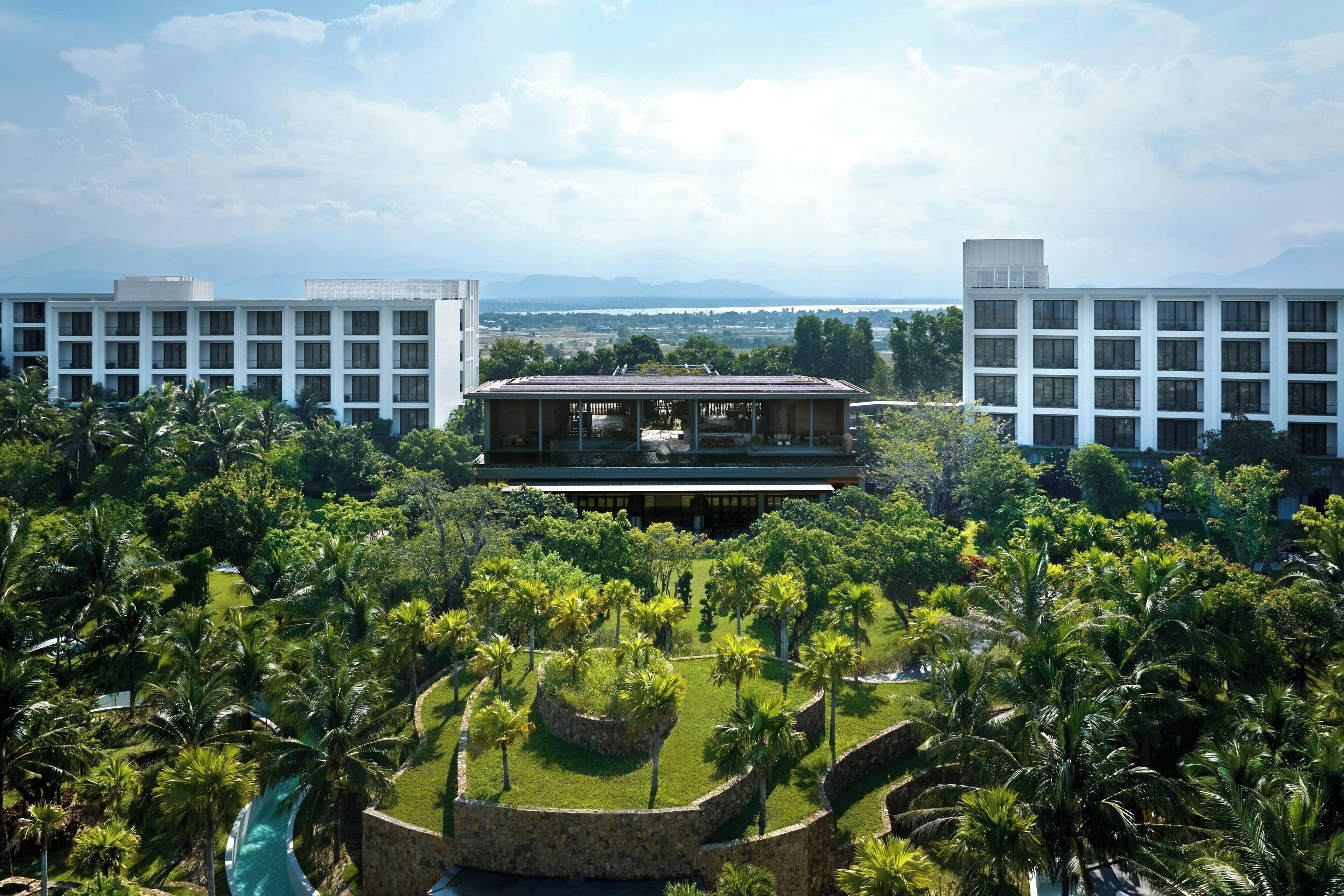 Un hotel con un edificio central rodeado de exuberante vegetación y palmeras.