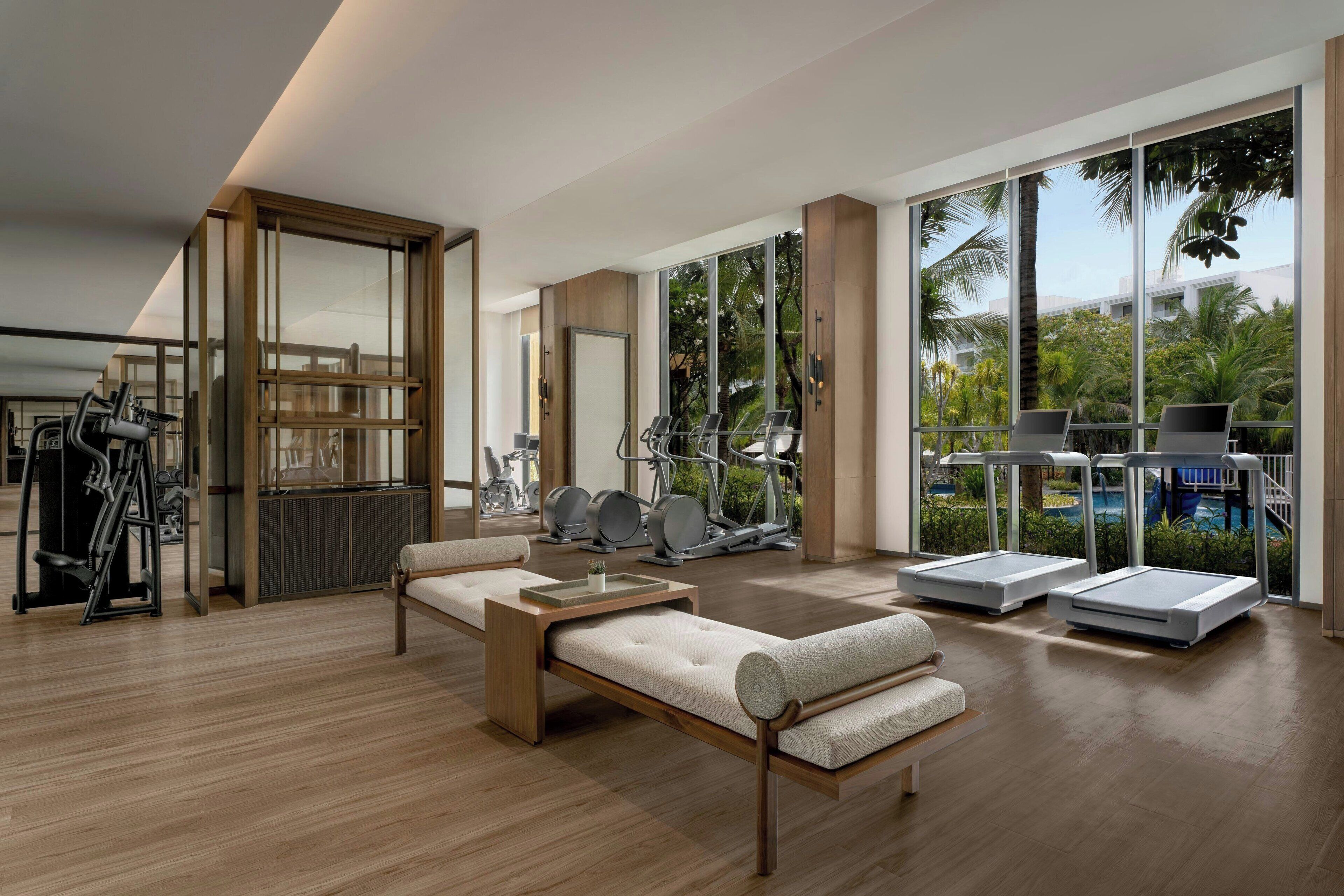 A modern gym with exercise equipment, a lounge area with a sofa, and large windows offering a view of the outdoors.