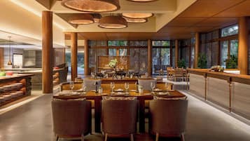 Un restaurante amplio con techos altos, ventanas grandes y un área de comedor central con una barra larga y varias mesas.
