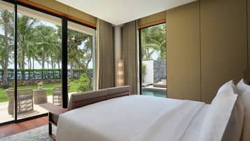 Un dormitorio con una cama grande, un área de descanso con vista a una piscina y palmeras, y un ventanal amplio.