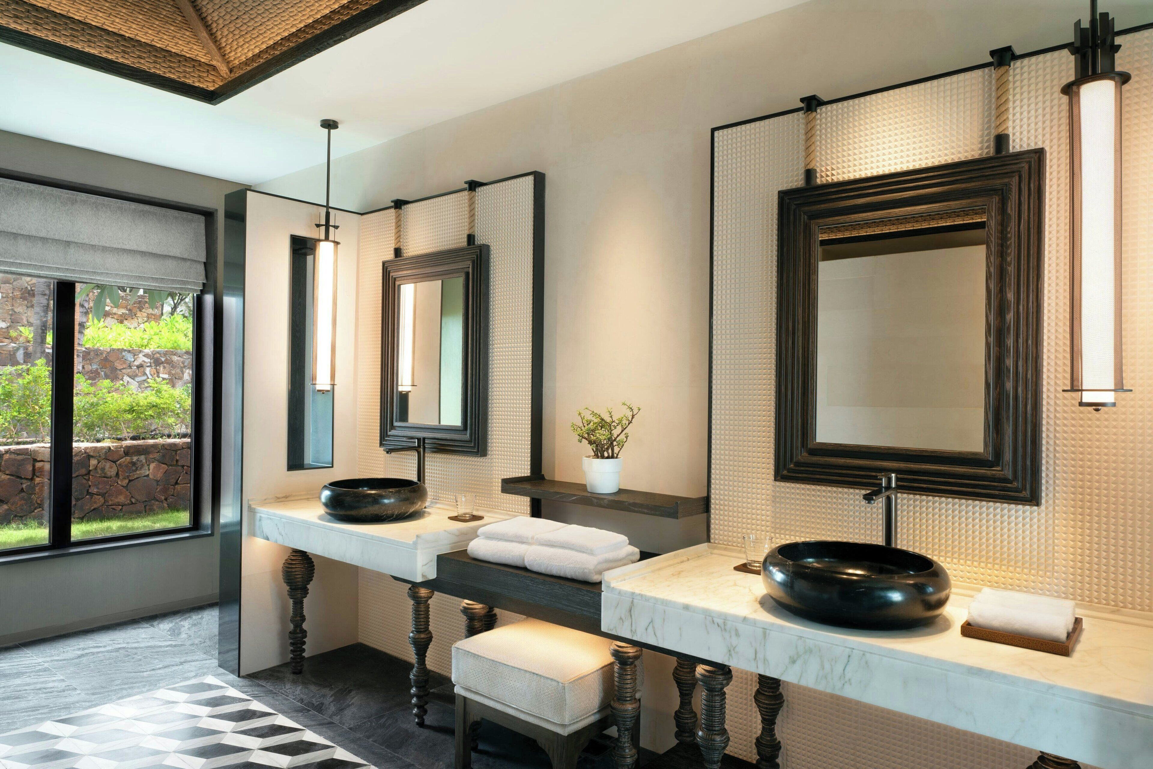 A modern bathroom with a large window, two sinks with round black bowls, and a large mirror.