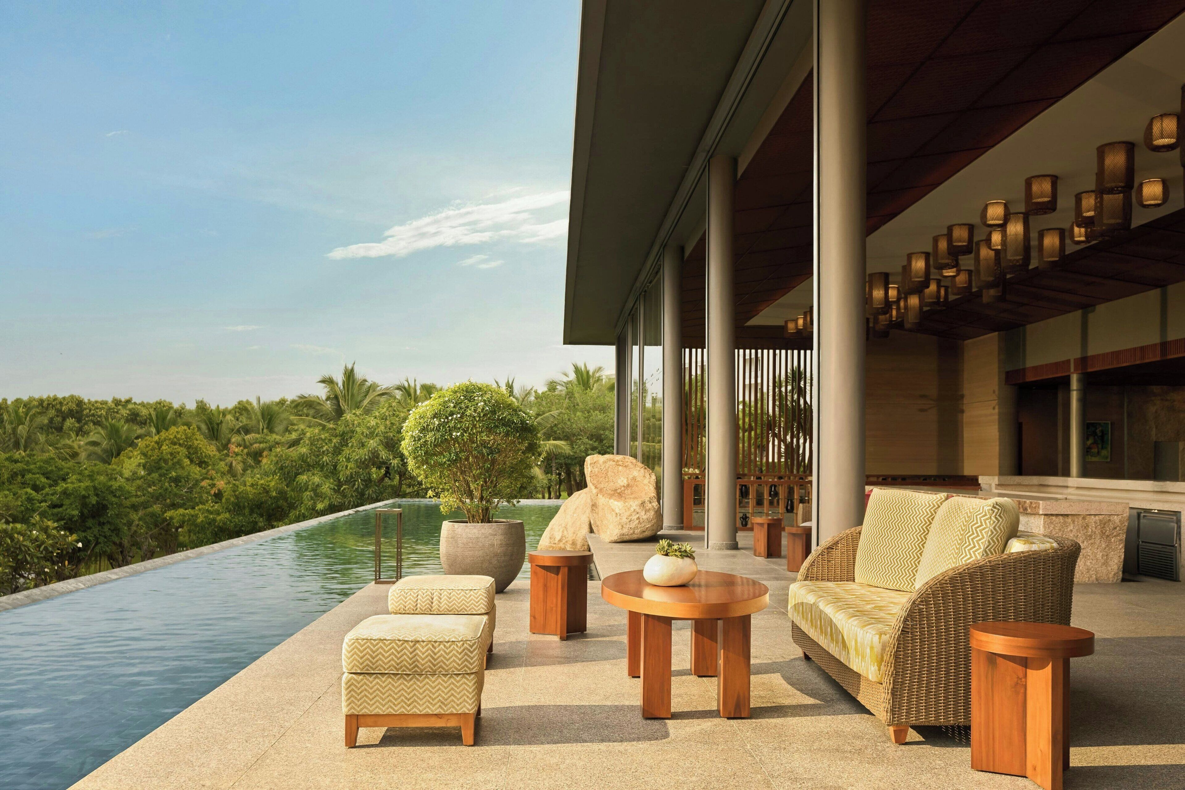 A poolside area with outdoor furniture, a large potted plant, and a view of a lush landscape.