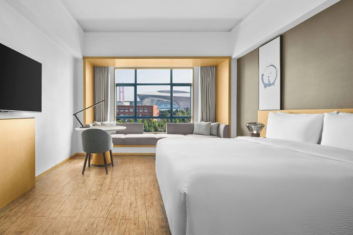 Een hotelkamer met een groot bed, een bureau, een stoel, een televisie en een raam met uitzicht op de stad.