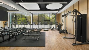 A gym with treadmills, dumbbells, and weight machines, large windows with a view of trees, and a wooden floor. - Fairfield By Marriott Shunde (Foshan)