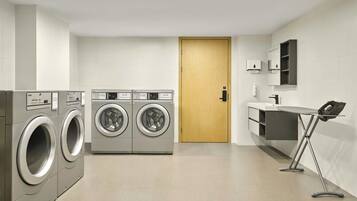 A modern laundry room with two front-loading washing machines, a wooden door, and a small ironing station.