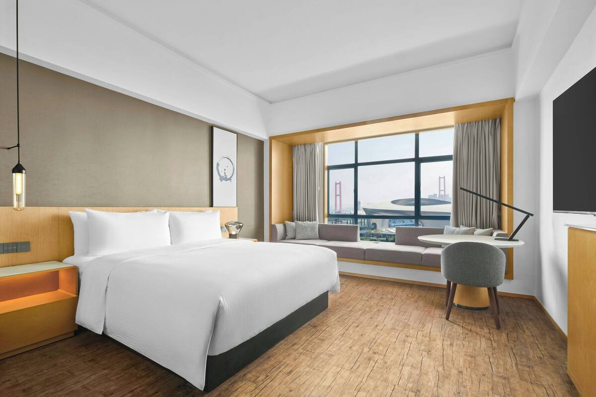 Hotelkamer met een groot bed, een zithoek bij het raam, een bureau en uitzicht op een brug.