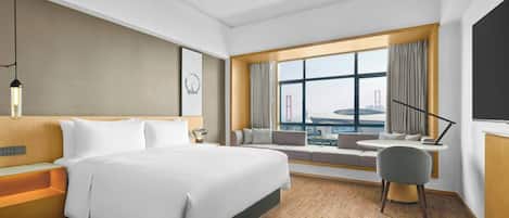 A hotel room with a large bed, a seating area by the window, a desk, and a view of a bridge.