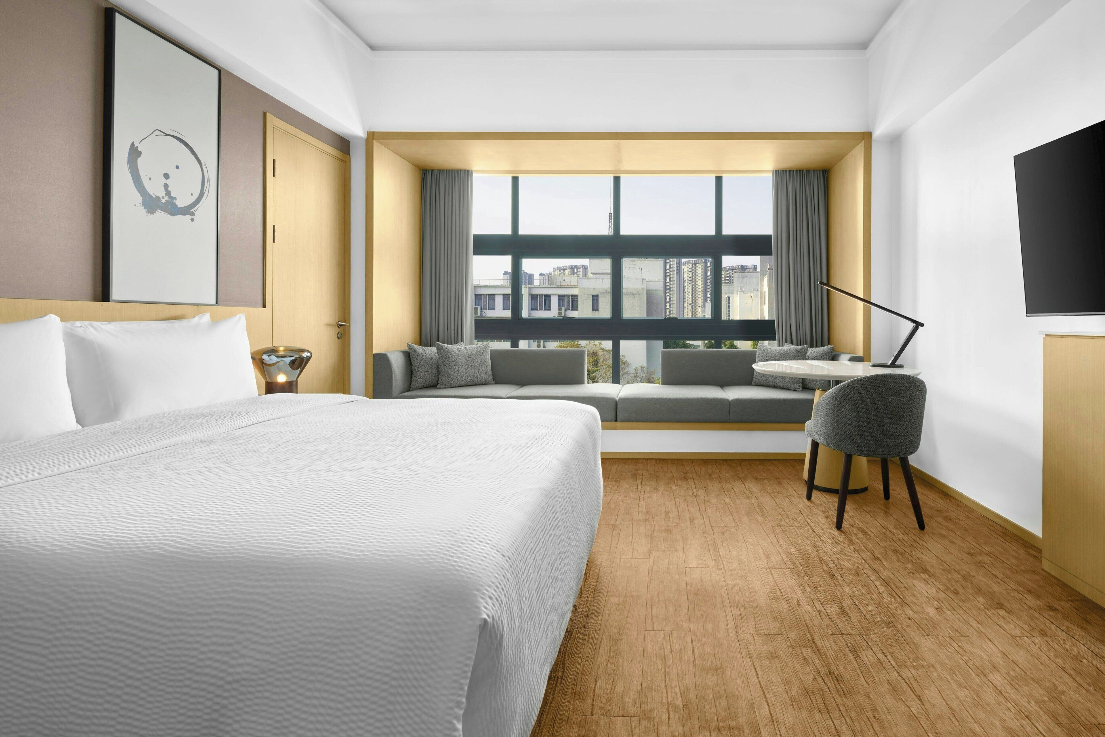Quarto de hotel com uma cama grande, um sofá, uma mesinha, uma cadeira e uma televisão.