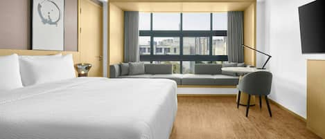 A hotel room with a large bed, a sofa, a small table, a chair, and a TV.