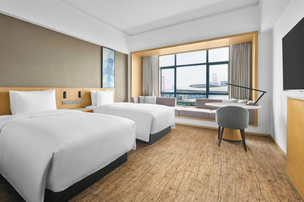 Een hotelkamer met twee bedden, een bureau, een stoel, een groot raam met uitzicht en een televisie.