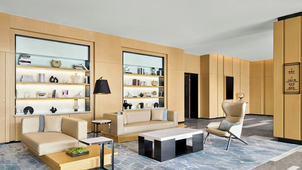 A modern hotel lobby with a sofa, armchairs, a coffee table, and a bookshelf filled with books and decorative items. - Fairfield By Marriott Shunde (Foshan)