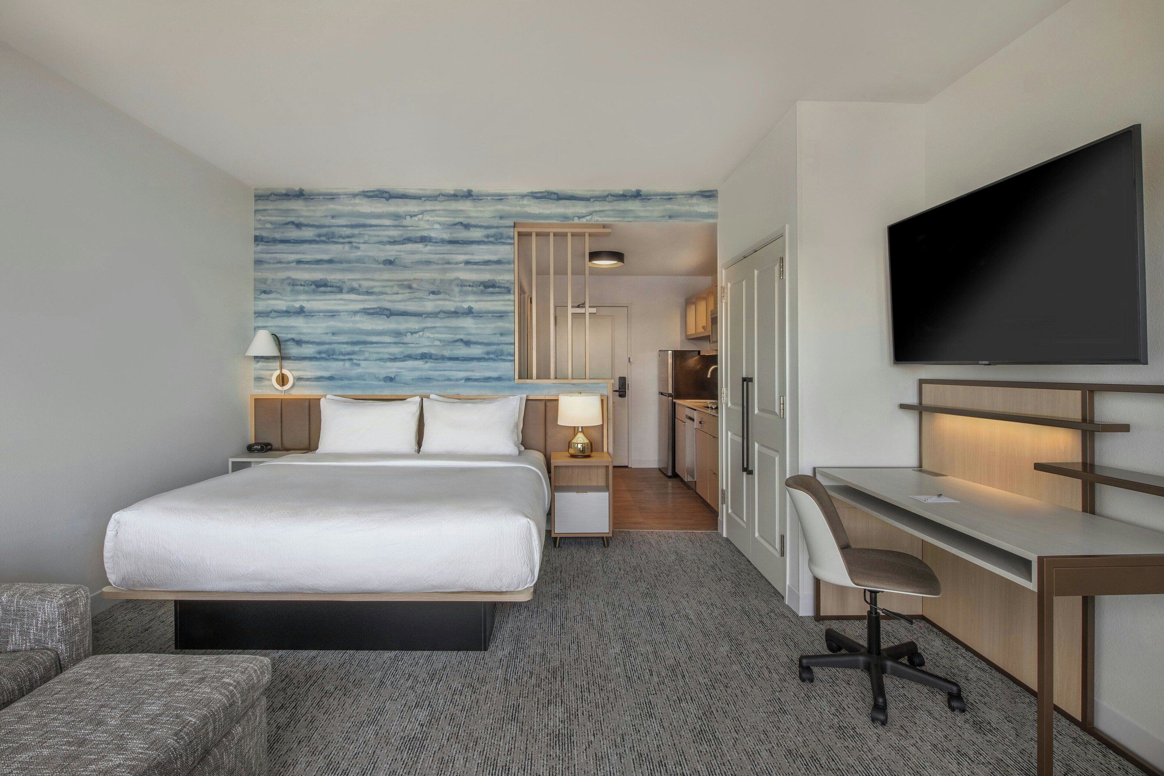 Hotelkamer met een bed, een bureau, een televisie, een bureaulamp, een stoel en een muur met een blauw abstract ontwerp.