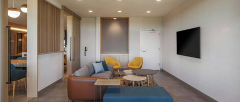 A modern living room with a sofa, two armchairs, a coffee table, and a TV mounted on the wall.
