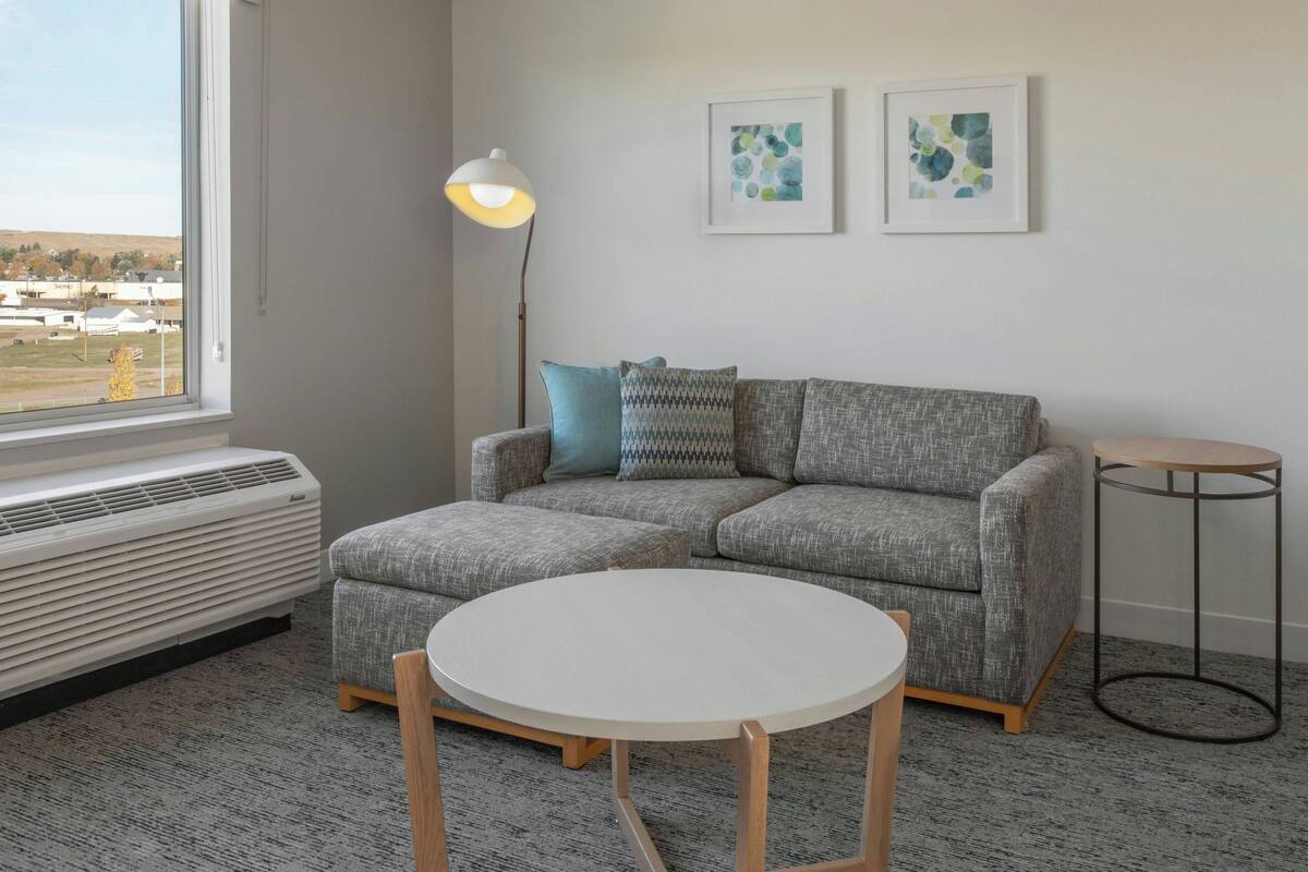 Un salon moderne avec un canapé gris, une table ronde blanche et un lampadaire.