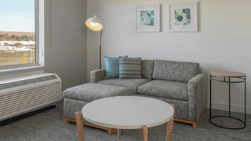 Een moderne woonkamer met een grijze bank, een ronde witte tafel en een staande lamp.