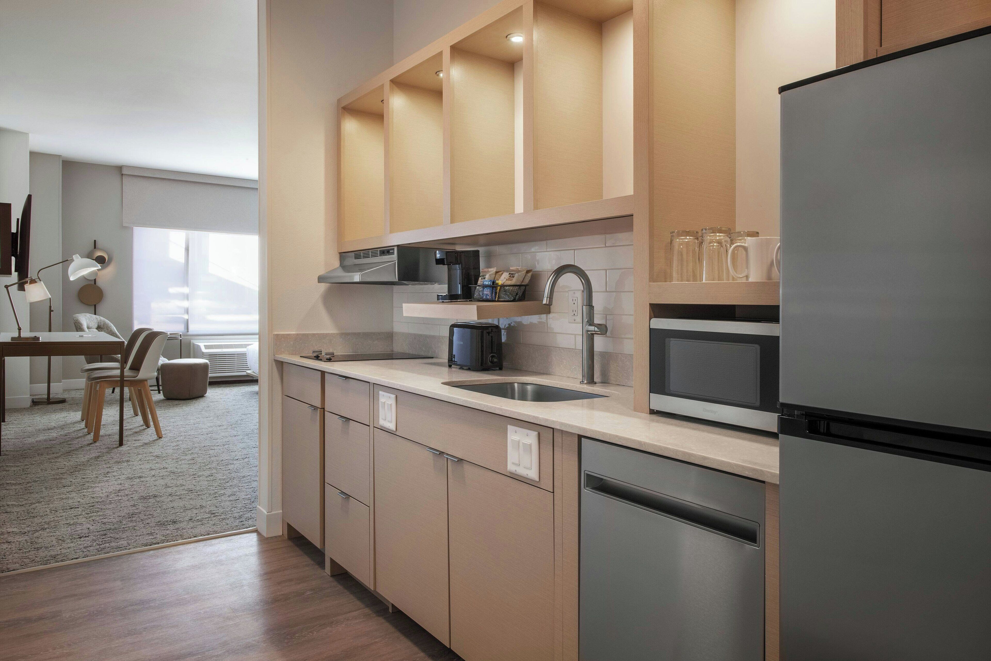 Una cocina moderna con lavavajillas, pileta y microondas integrado. Se observa un comedor con una mesa y sillas al fondo.