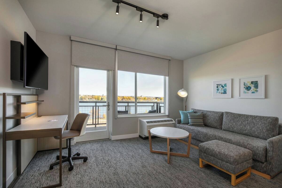 Un salon moderne avec un bureau, un canapé et une vue sur une étendue d’eau grâce à de grandes fenêtres.