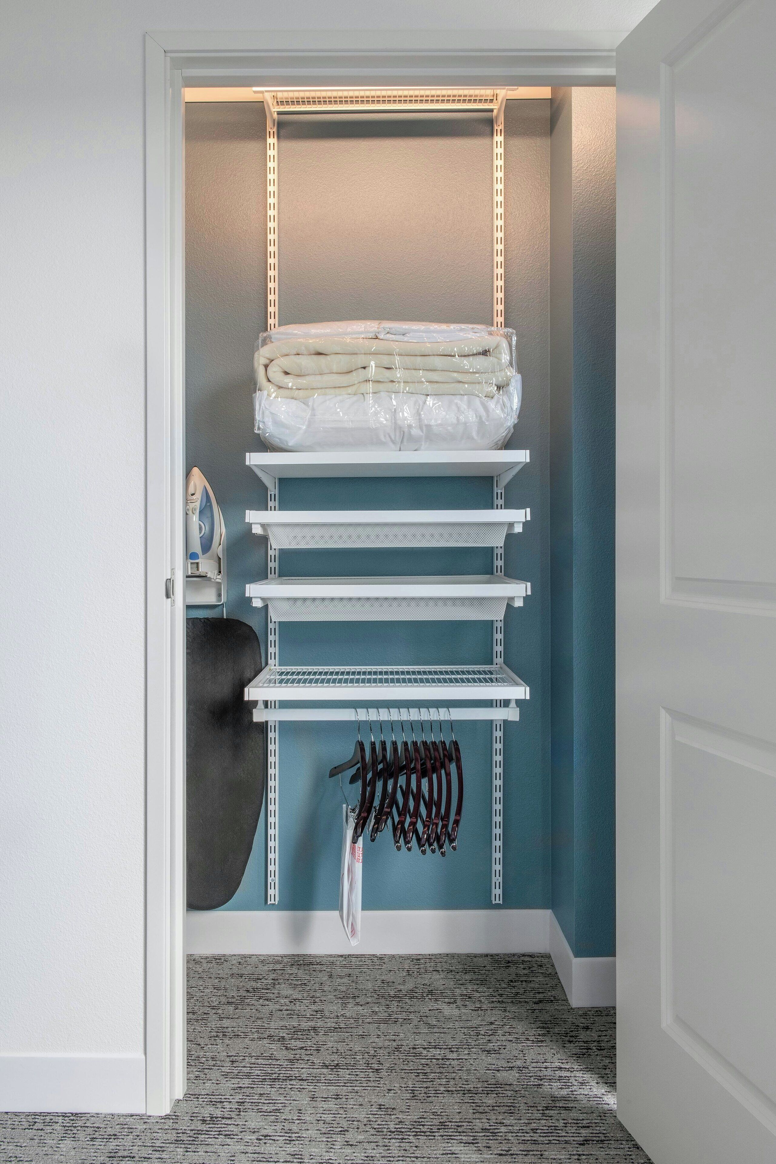 A closet with shelves, an ironing board, and hanging clothes.