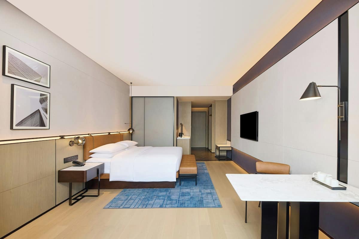 Una habitación de hotel moderna con cama, mesita de noche, lámpara y una pequeña mesa con tazas.