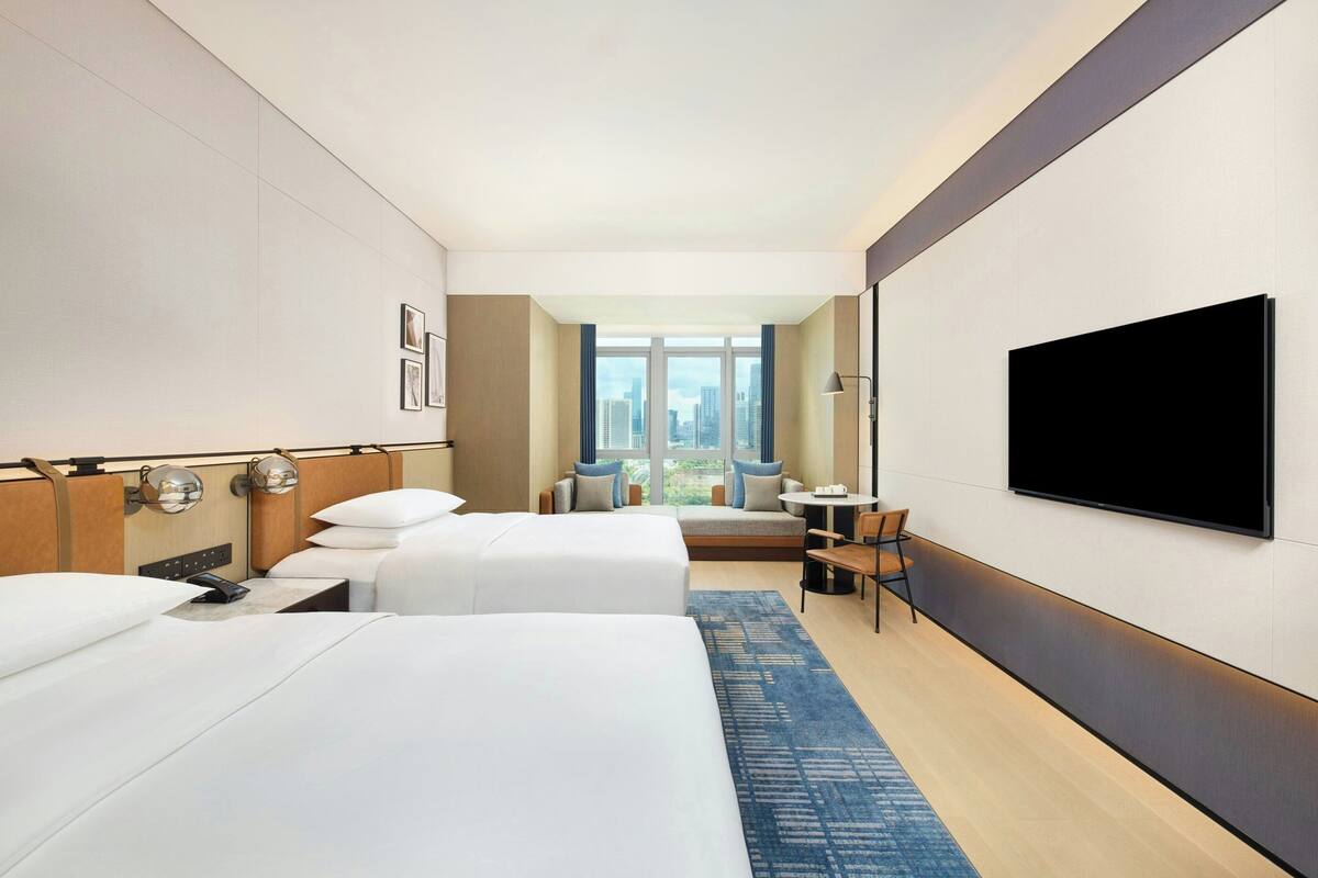 Habitación de hotel con dos camas, televisión, escritorio y vista a la ciudad.