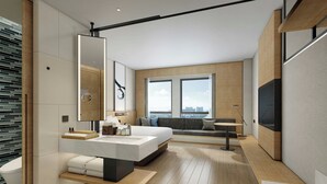 Una habitación de hotel moderna con una cama grande, un área de descanso, un ventanal amplio y un televisor.