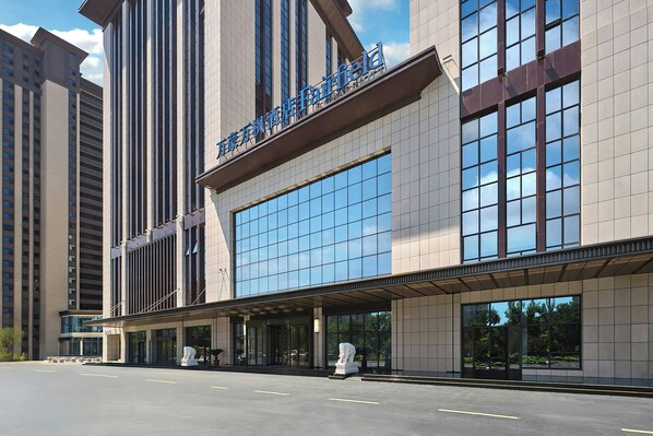 A modern hotel with a large glass facade, a prominent entrance, and a parking area.