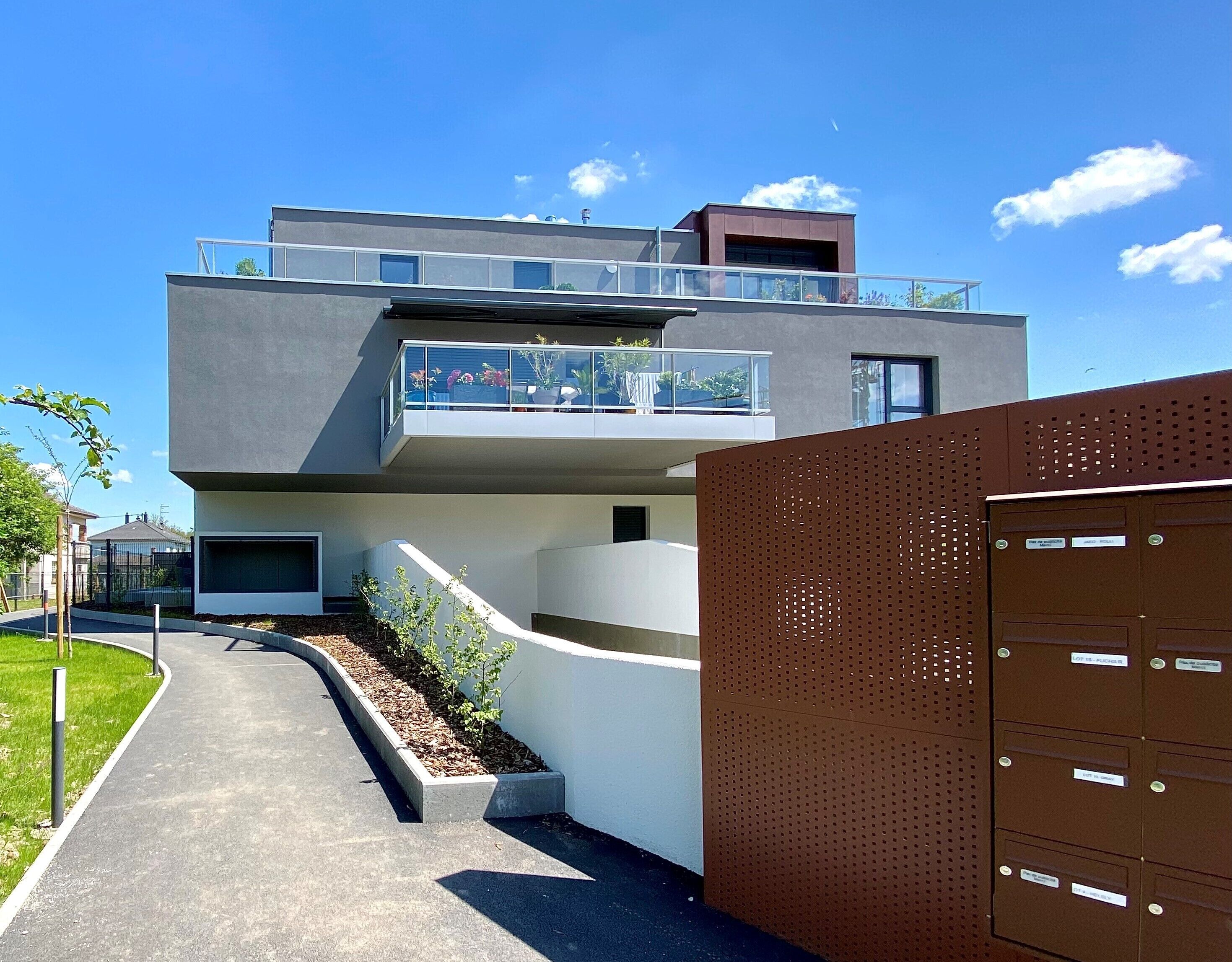 A modern two-story building with a flat roof, large windows, and a balcony.