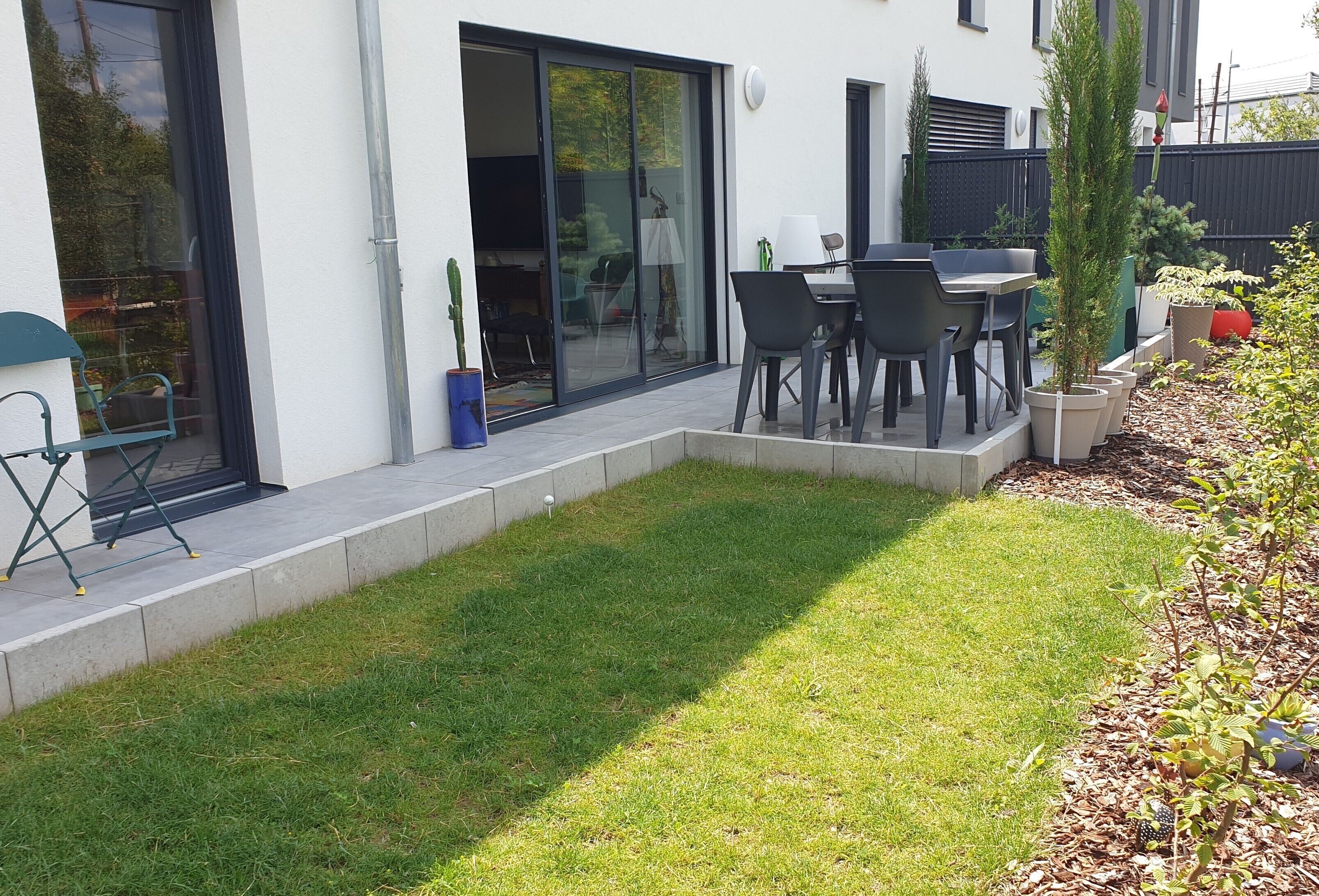 Et moderne hus med terrasse, spiseplads og en lille have.