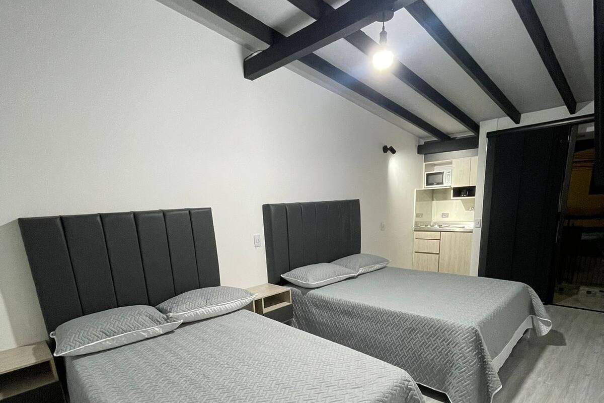 A bedroom with two beds, a kitchenette, and a staircase.