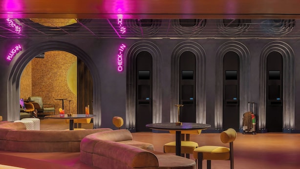 A modern lounge area with plush seating, a check-in desk, and a neon sign. - Moxy London Piccadilly Circus (London)
