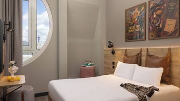 Ein Hotelzimmer mit einem Bett, einem Schreibtisch mit Lampe, einem Fenster mit Blick und zwei Bildern an der Wand.