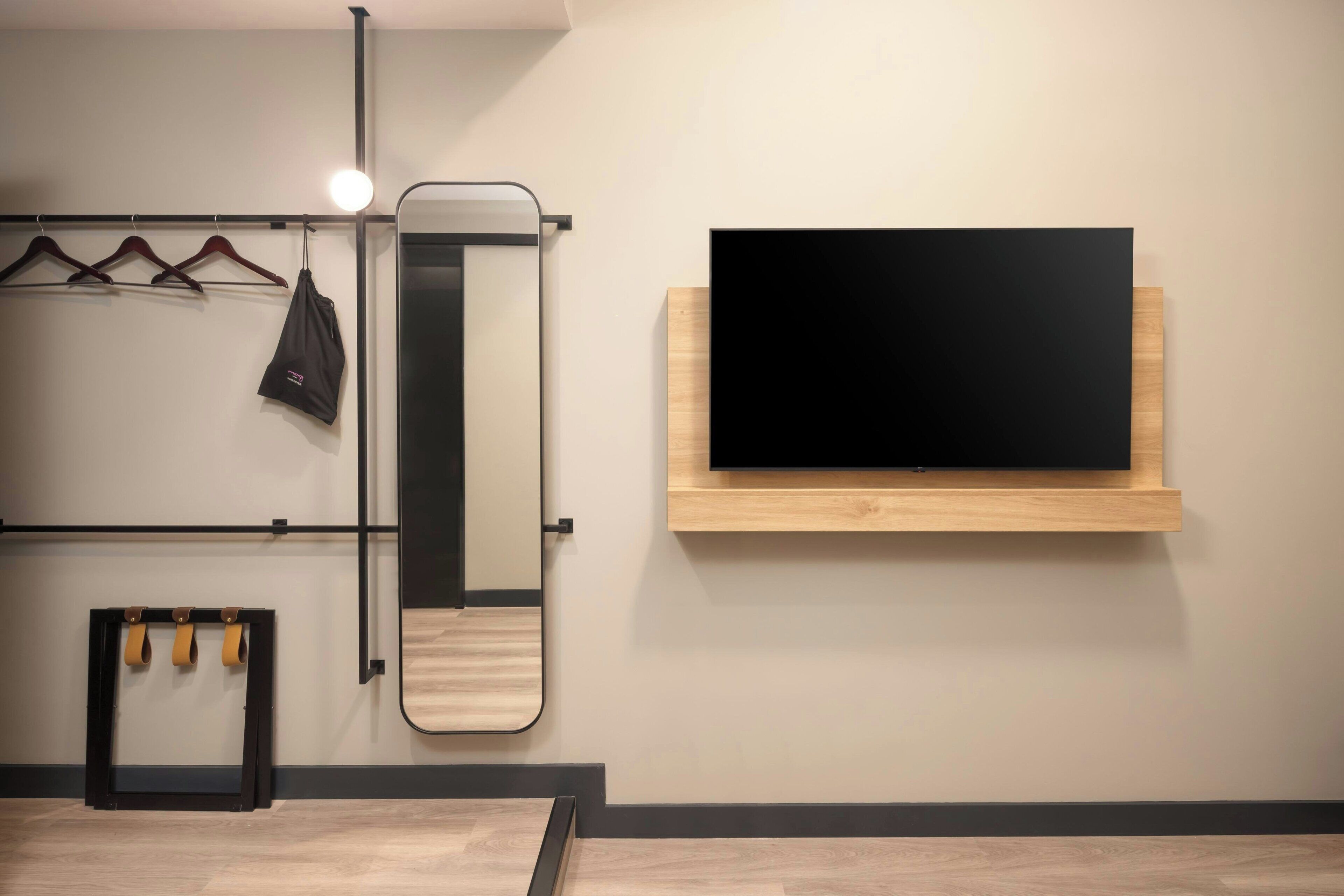 Ein modernes Zimmer mit einem Wandfernseher, einem Spiegel und einer Kleiderstange.