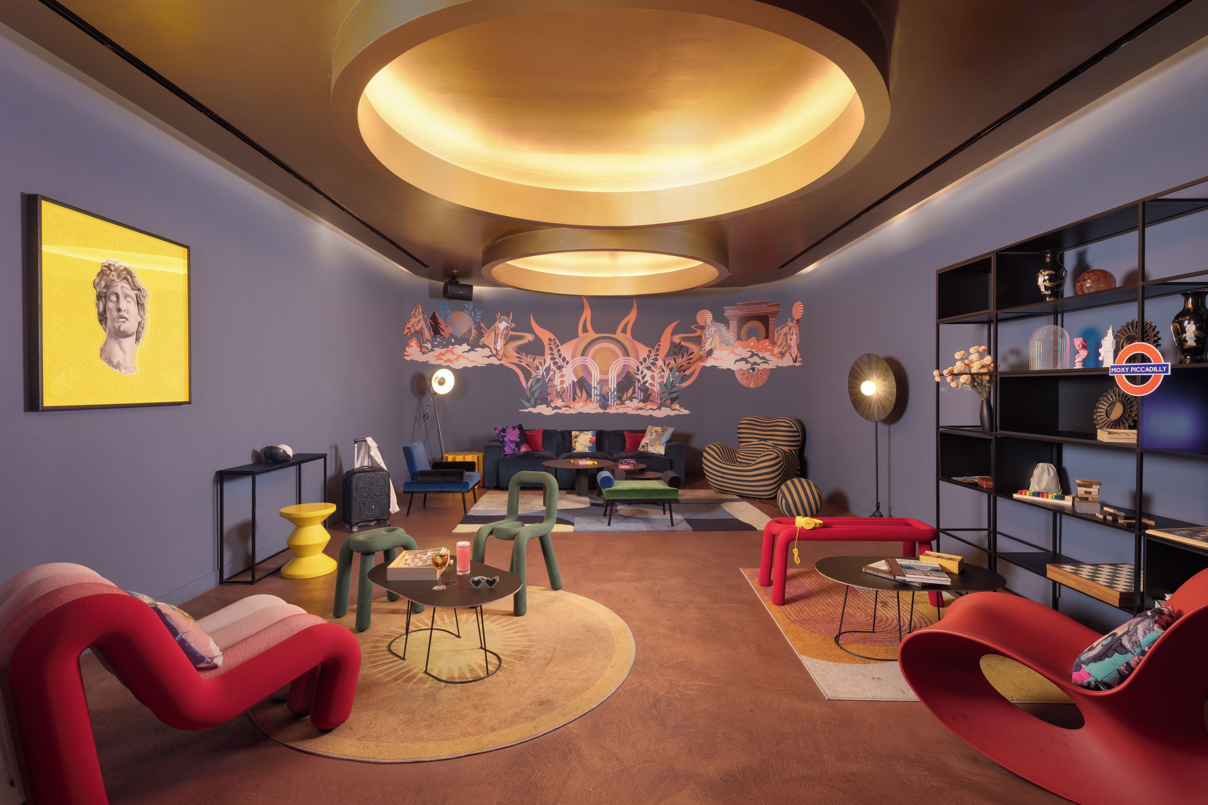 A modern living room with a round ceiling light, a mural, and a bookshelf.