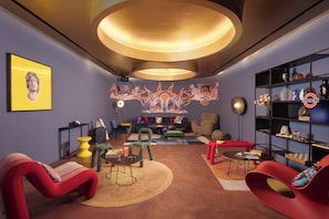 A modern living room with a round ceiling light, a mural, and a bookshelf. - Moxy London Piccadilly Circus (London)