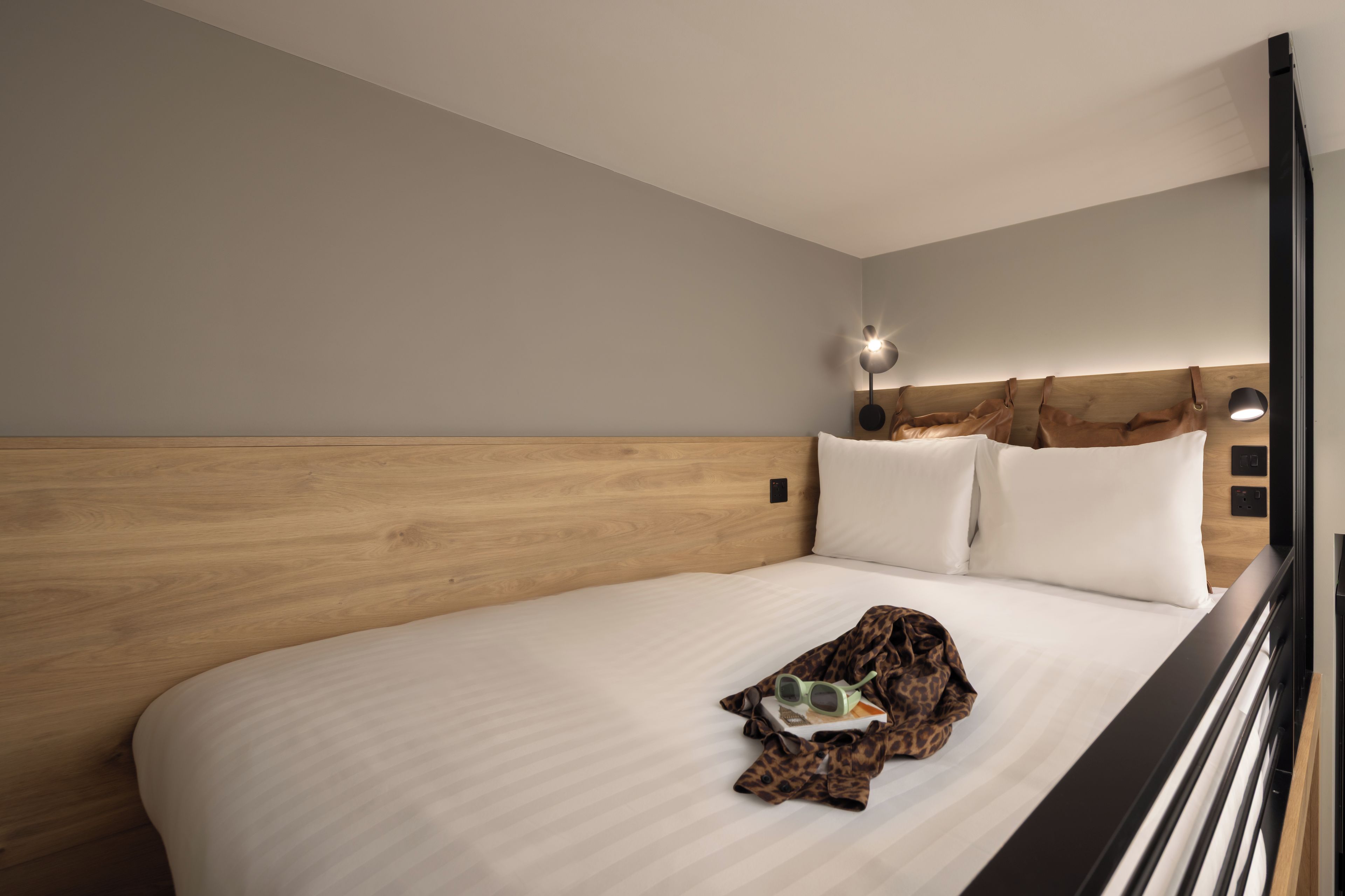 A modern hotel room with a wooden headboard, a large bed, and a nightstand with a lamp.