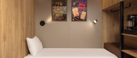 A compact room with a single bed, a coffee machine, and two framed posters on the wall.