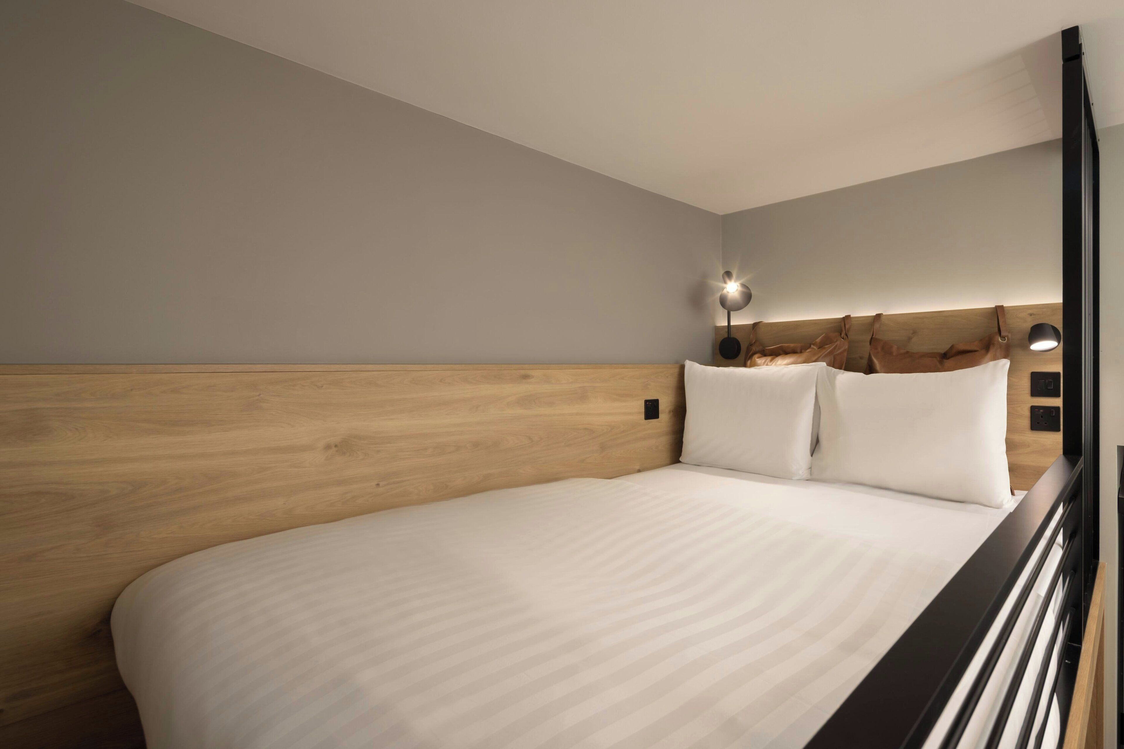 Una habitación de hotel moderna con cabecera de madera, una cama grande y una mesita de noche con una lámpara.