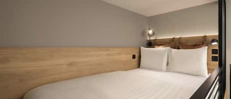 Et moderne hotelværelse med en træsenggavl, en stor seng og et natbord med en lampe.