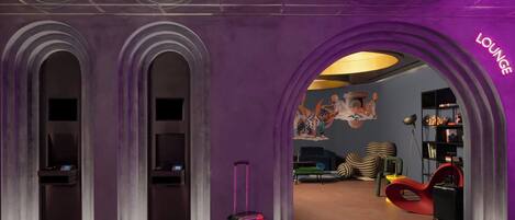 A purple archway labeled "Lounge" leading to a room with a mural, a red chair, and a black suitcase.