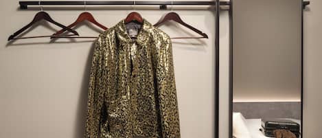 A bed with a suitcase and a leopard print garment hanging on a rack.