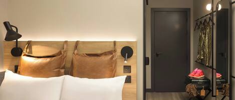 Una habitación de hotel moderna con una cama, una mesita de noche, una lámpara, un espejo y un armario.