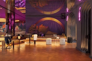 Um saguão de hotel moderno com um grande mural, áreas de estar e um carrinho de bagagem.