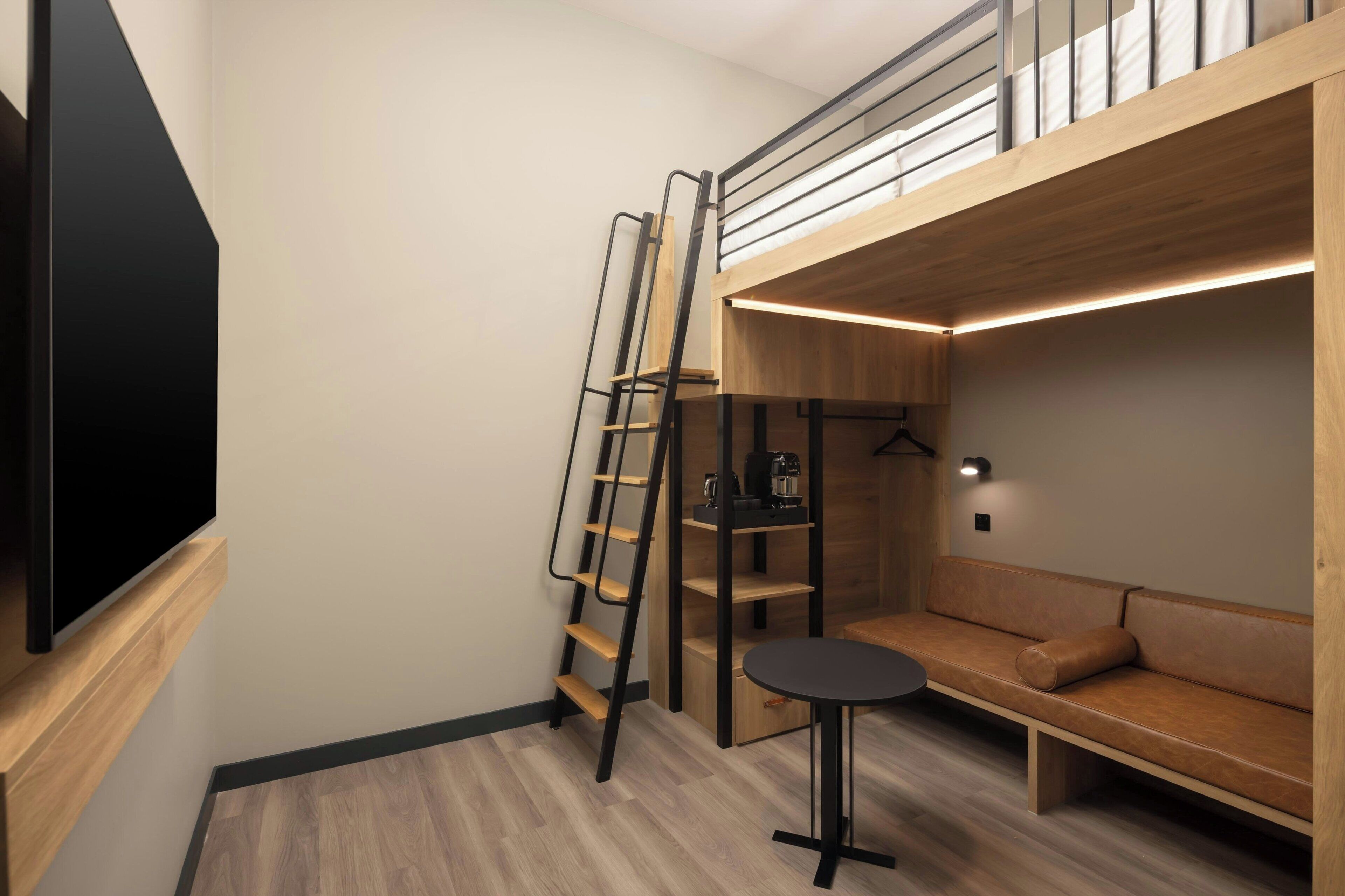 Una habitación pequeña con una cama litera, una mesita, un sofá y un televisor fijado a la pared.