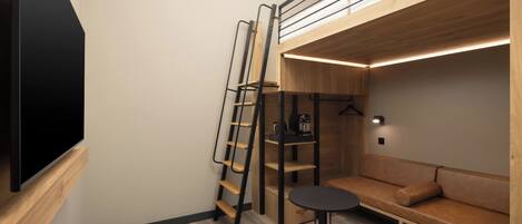 A compact room with a bunk bed, a small table, a sofa, and a TV mounted on the wall.