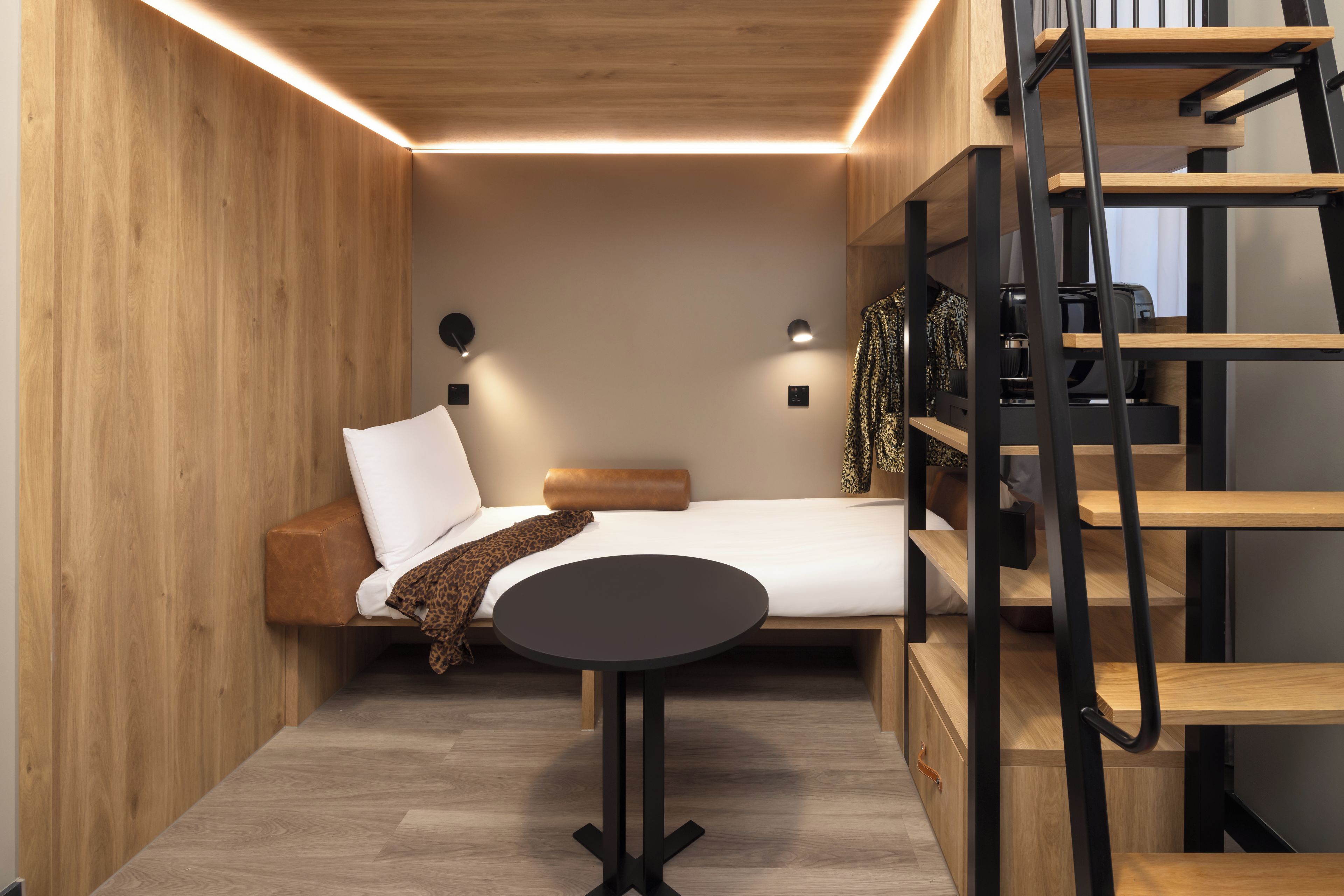A compact room with a bed, a small table, and a built-in shelving unit.