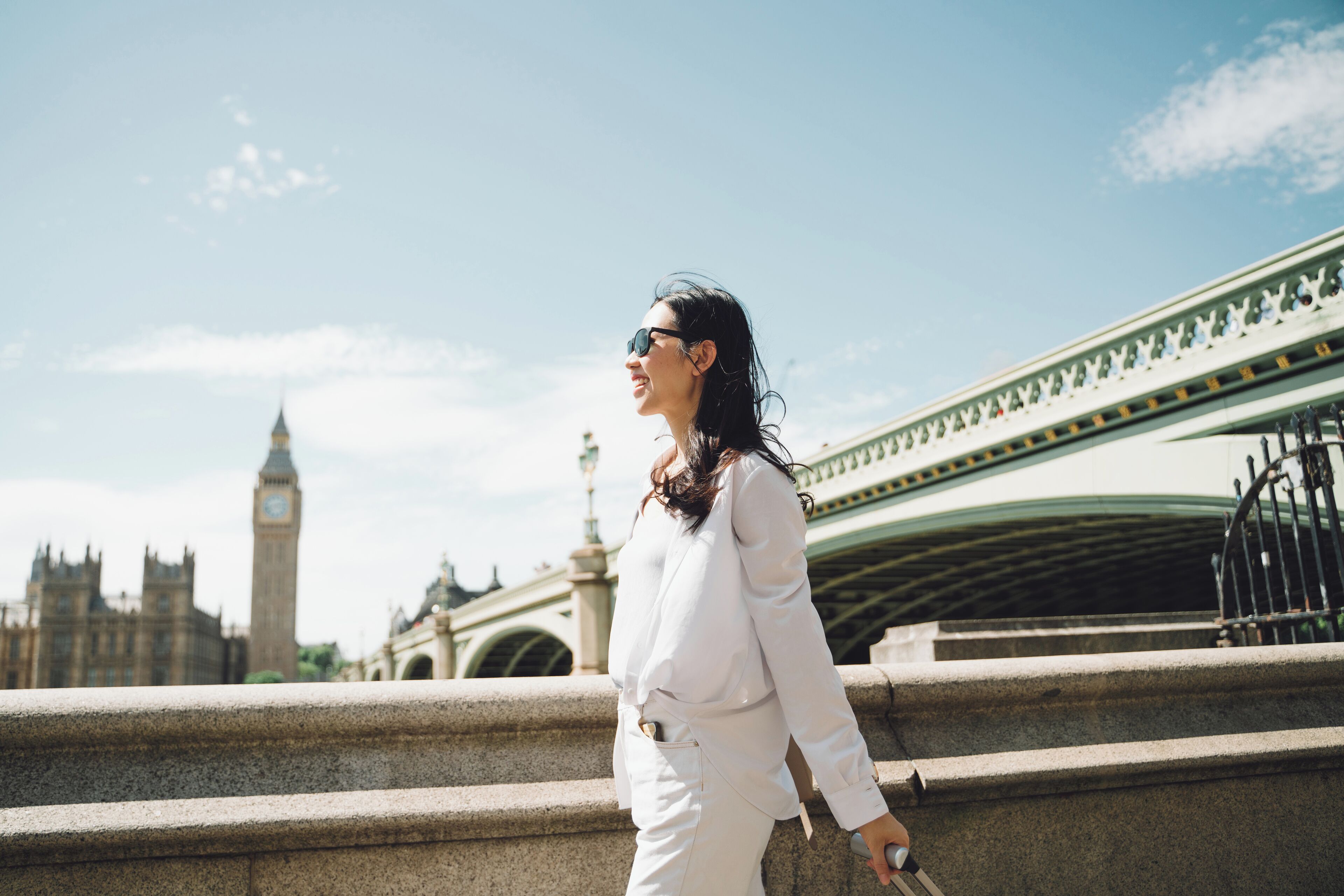 A person in a white outfit walking on a stone bridge with a historic building in the background.