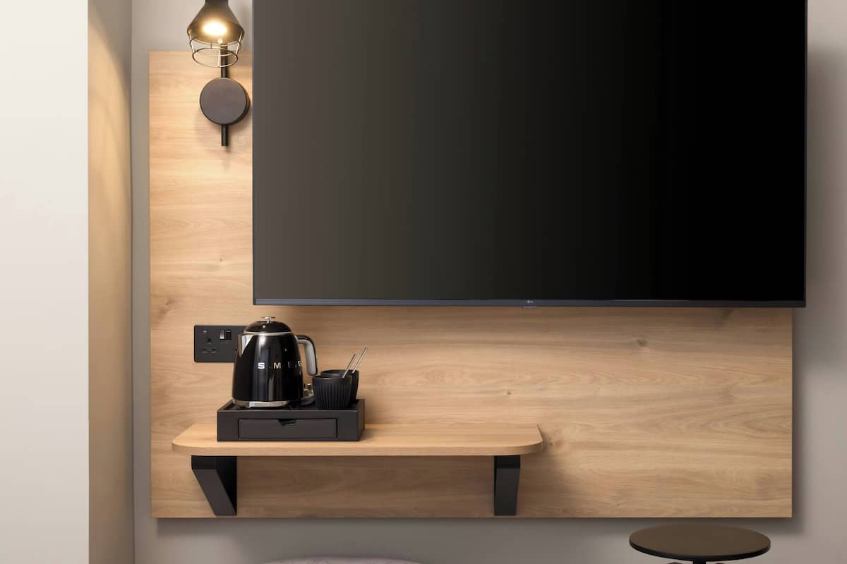 A modern room with a mounted TV, a coffee maker, and a small table.