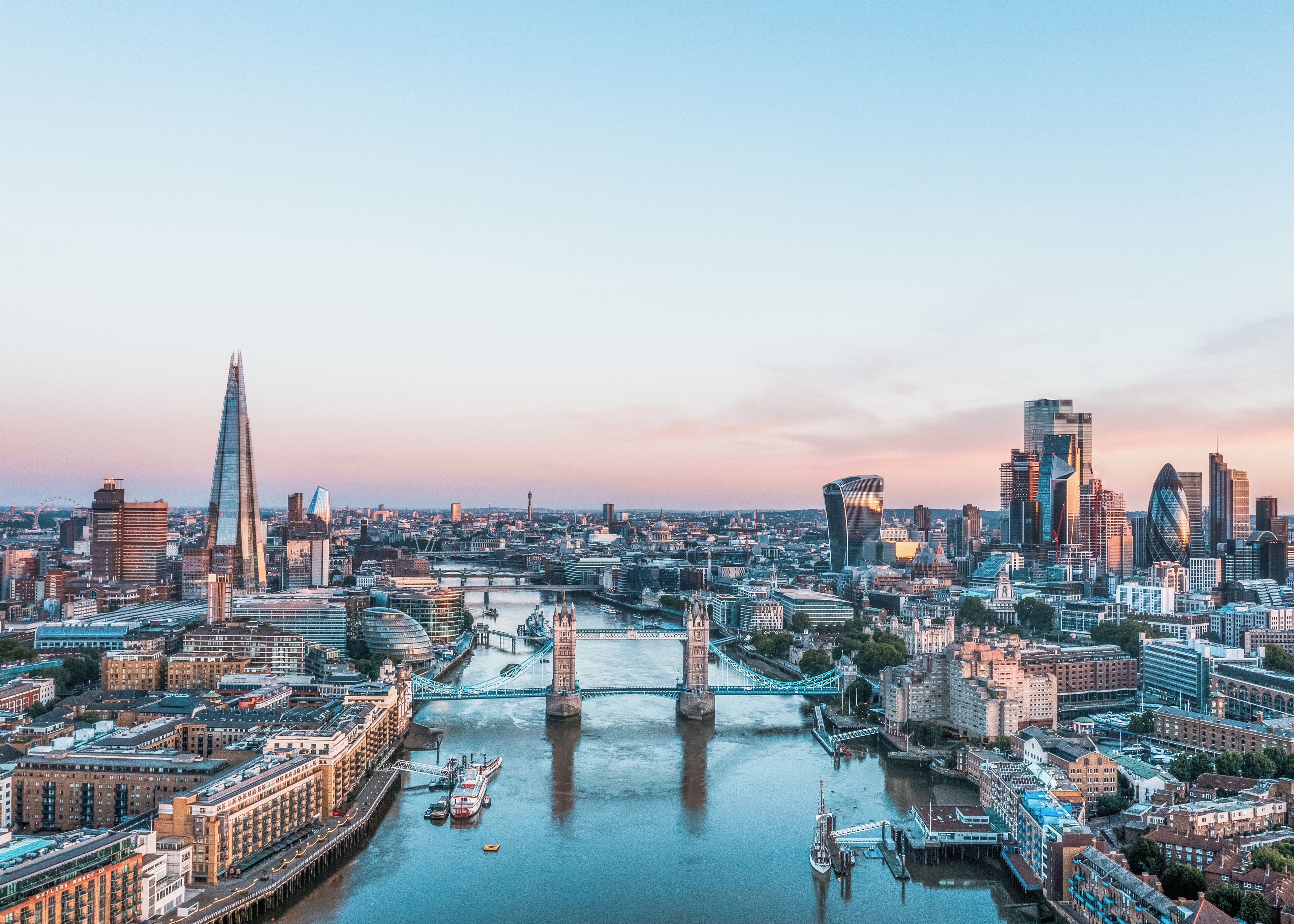 Een panoramisch uitzicht op een stadsgezicht met opvallende moderne wolkenkrabbers, een rivier en een historische brug.