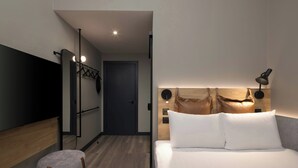 A modern hotel room with a bed, a bedside lamp, a wall-mounted TV, and a wooden headboard. - Moxy London Piccadilly Circus (London)