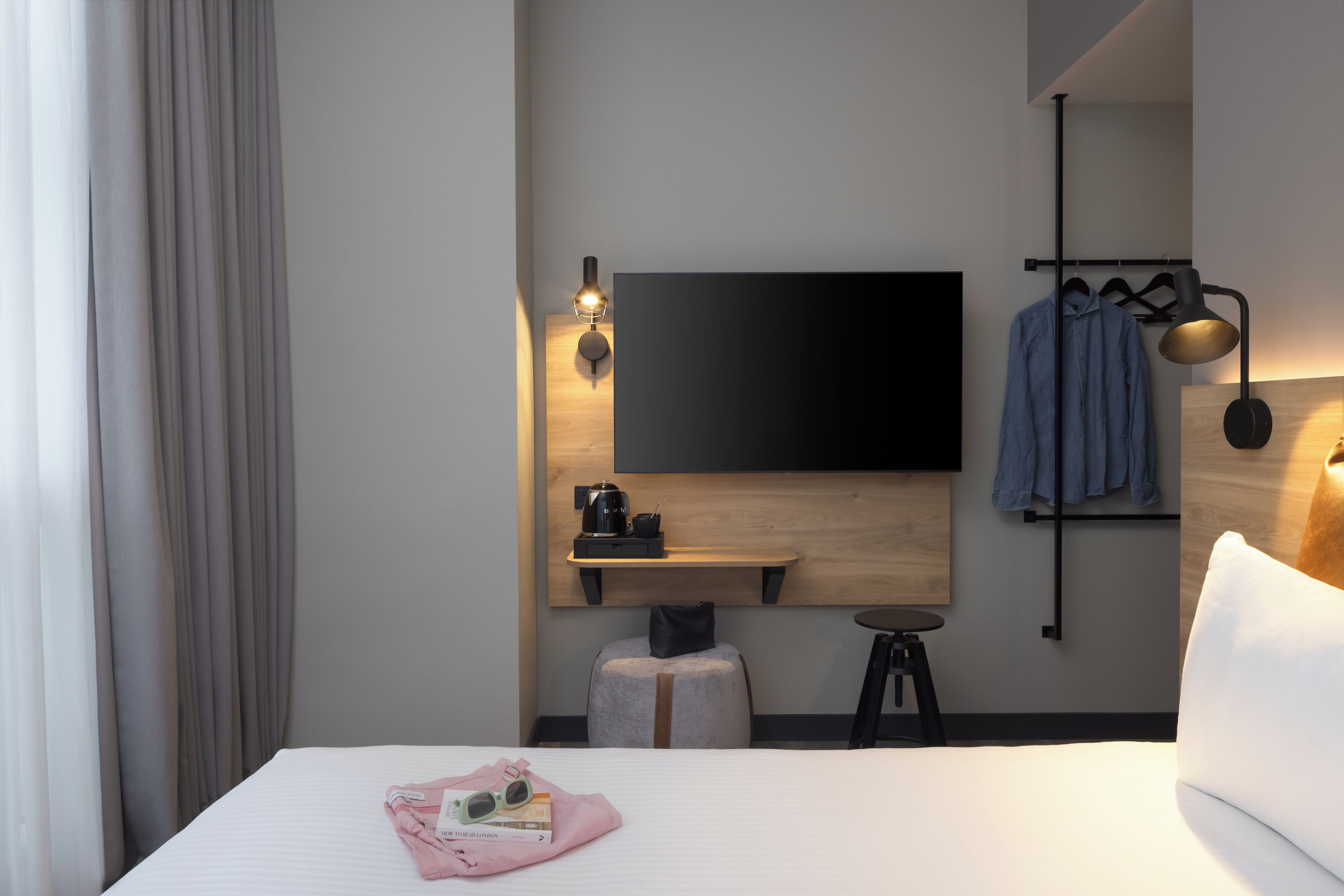 Une chambre d’hôtel équipée d’un lit, d’un téléviseur à écran plat fixé au mur, d’une petite table avec une machine à café et d’un porte-manteau mural.